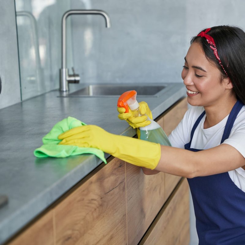 Happy young woman, cleaning lady smiling while cleaning the kitchen